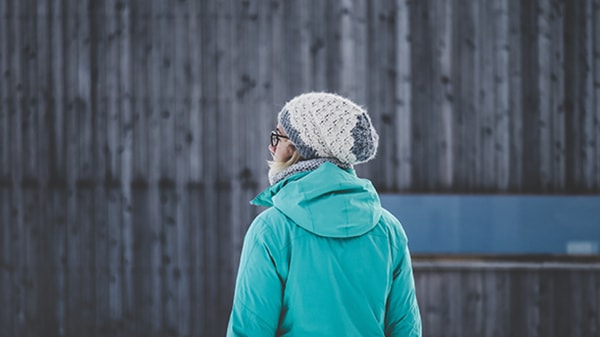 A girl wearing a scarlet jacket, a colorful hat, and glasses is seen from behind